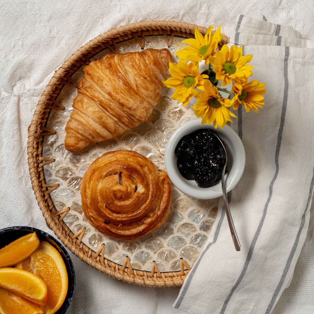 Breakfast setting with pastries, jam, and flowers on a textured surface
