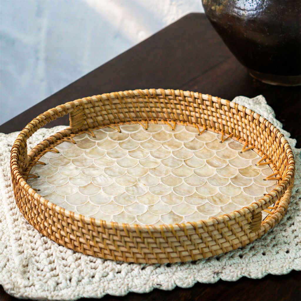 A round woven rattan tray with a scalloped shell-patterned insert, resting on a white crocheted doily over a dark wooden table.